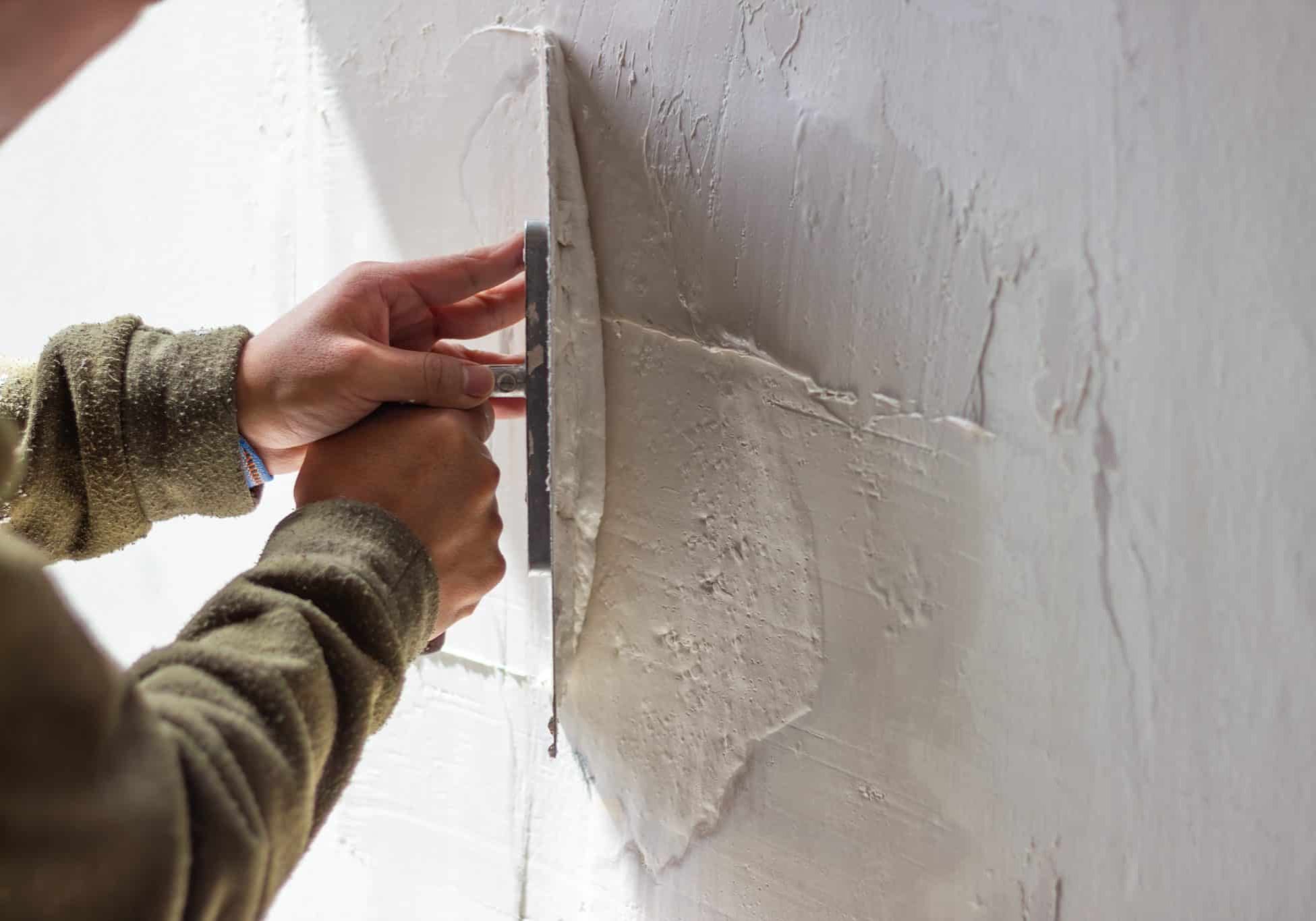 Construction worker is using a trowel to apply plaster on a wall, creating a textured surface during a home renovation or construction project